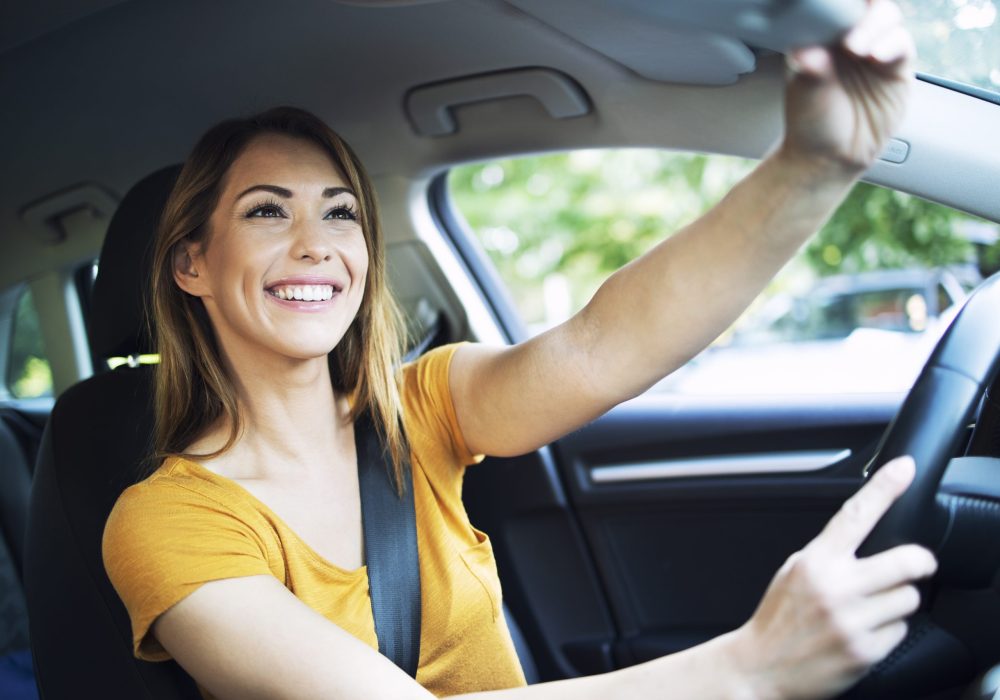 Car interior view of female woman driver adjusting mirrors before driving a car.